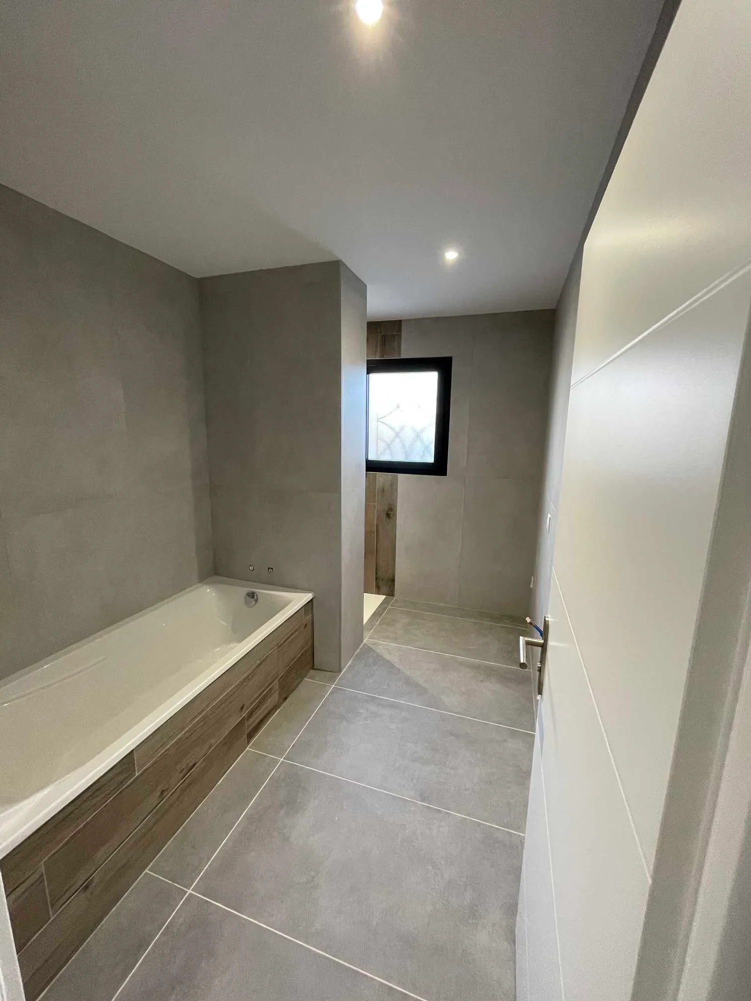 Salle de bain à Toulouse avec carrelage grand format gris effet béton et habillage de baignoire effet bois